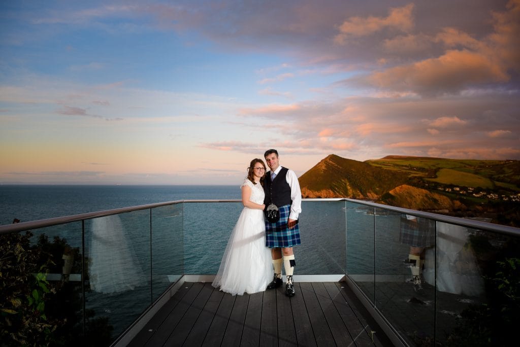 a man and woman posing for a picture on a balcony overlooking water