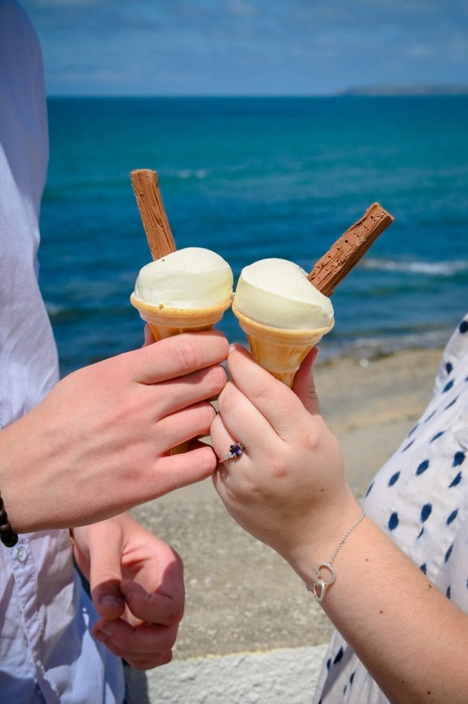 two hands holding ice cream cones on a beach
