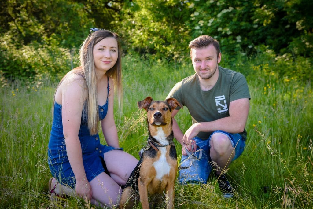 a man and woman sitting in grass with a dog