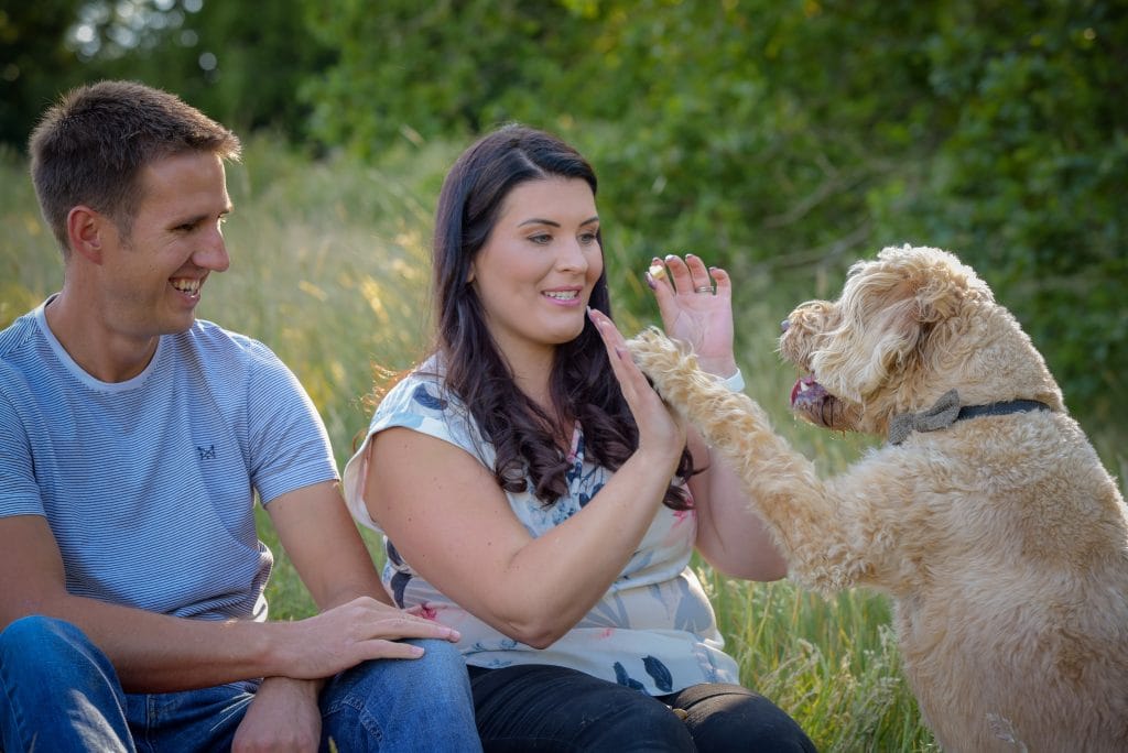 a man and woman sitting in grass with a dog