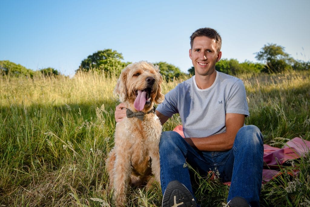 a man sitting with a dog in a grassy field