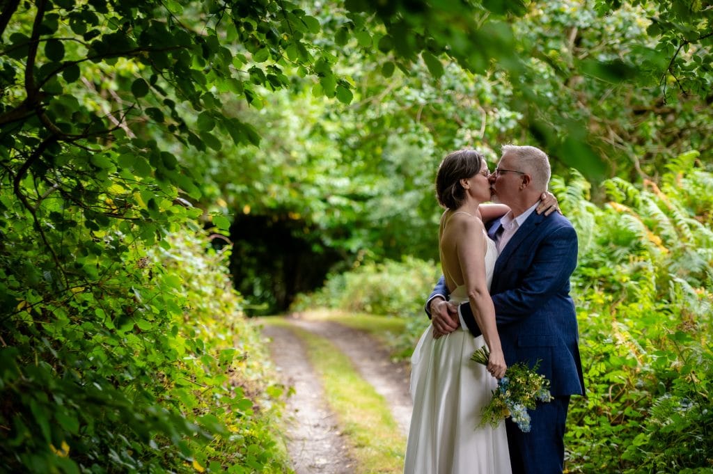 a man and woman kissing on a path with trees