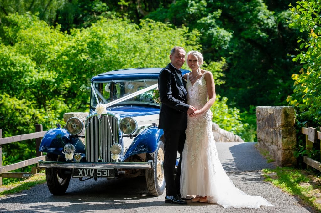 a man and woman in wedding dress standing in front of a blue car