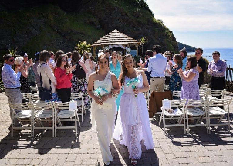 a group of women in white dresses walking down a walkway with chairs and a gazebo