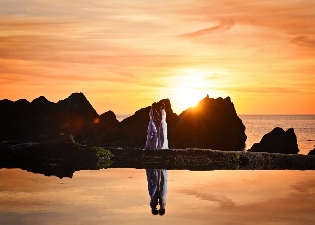 a group of people standing on a rock by water with a sunset
