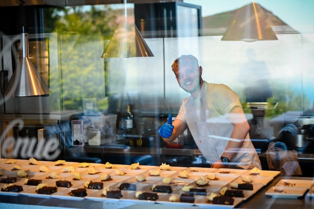 a man in a white shirt and blue gloves behind a counter with food